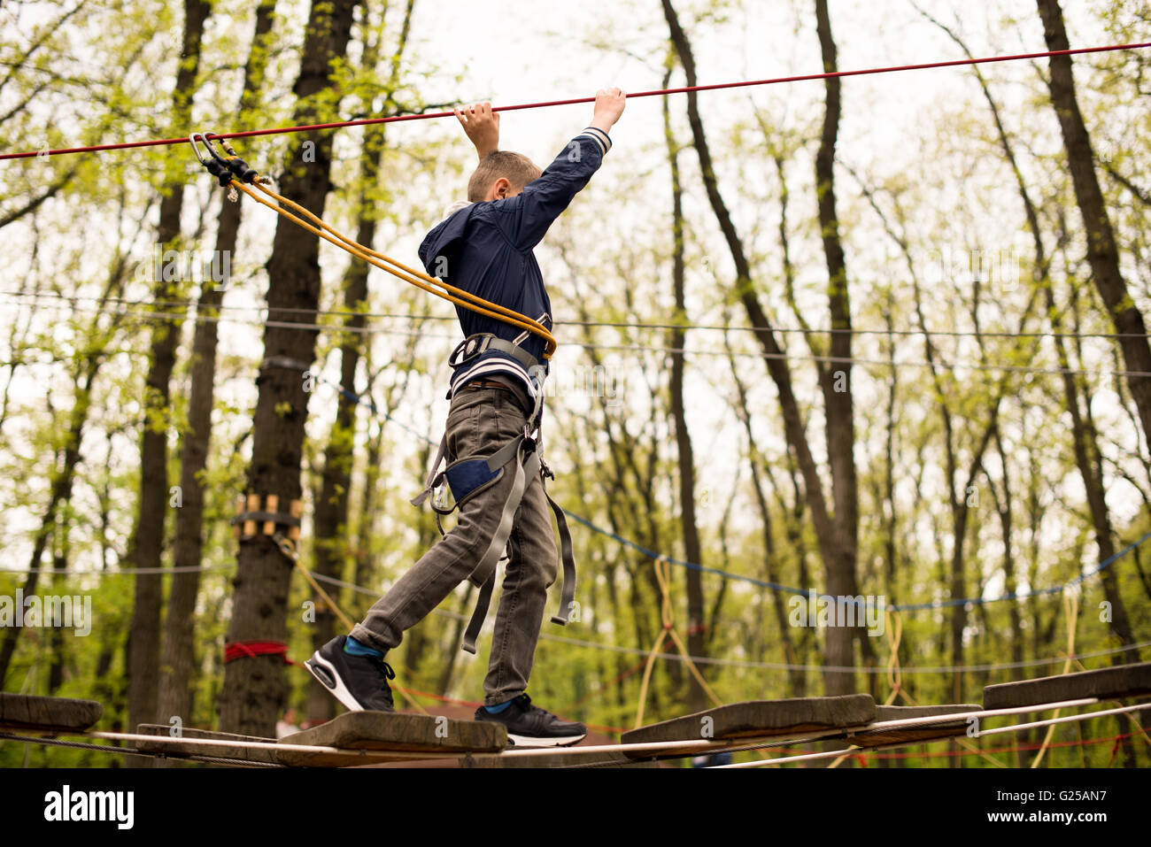 Ragazzo in corda elettrico sulla piattaforma di arrampicata nella struttura ad albero nel parco avventura Foto Stock