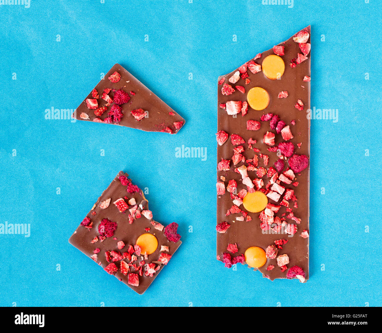 Vista dall'alto di un'arancia, fragola e lampone latte tavoletta di cioccolato rotto in tre pezzi su un fondo azzurro. Foto Stock