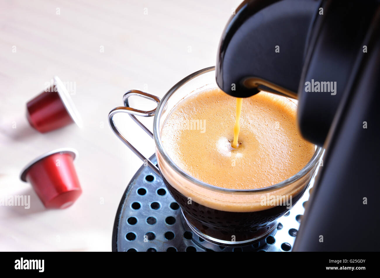 La macchina che serve caffè espresso in un bicchiere di vetro e due capsule sul tavolo Foto Stock