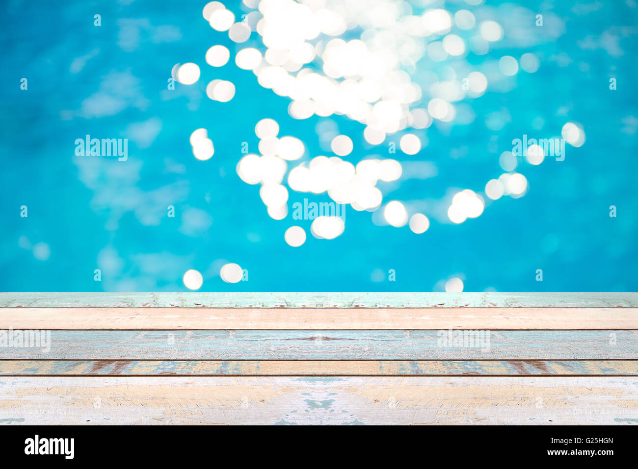 Legno in prospettiva del tavolo e soft focus bokeh di fondo gli effetti di luce su un variegato, blu sullo sfondo di acqua in piscina, display del prodotto Foto Stock