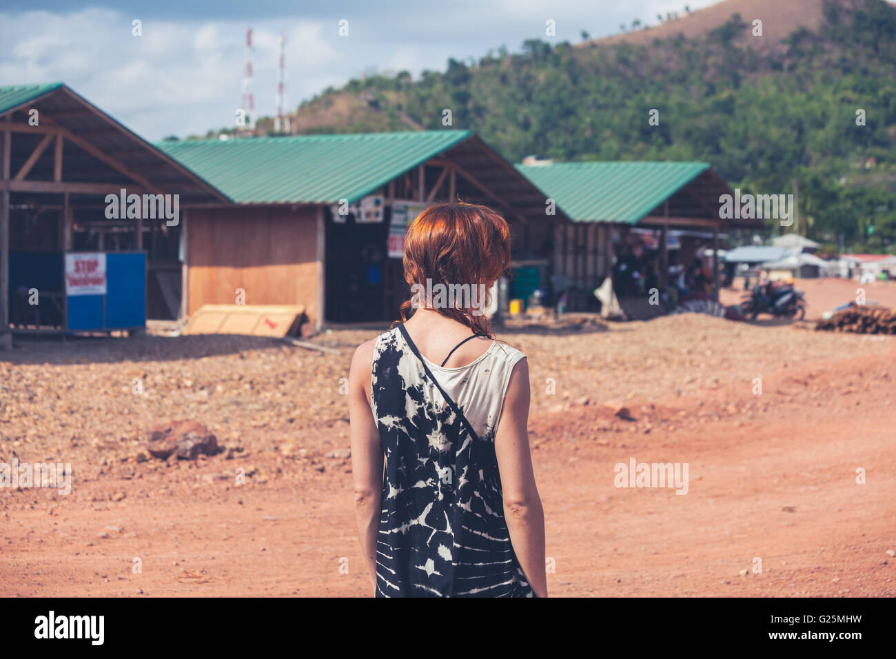 Una giovane donna caucasica è a piedi attorno a una piccola cittadina di un paese in via di sviluppo Foto Stock