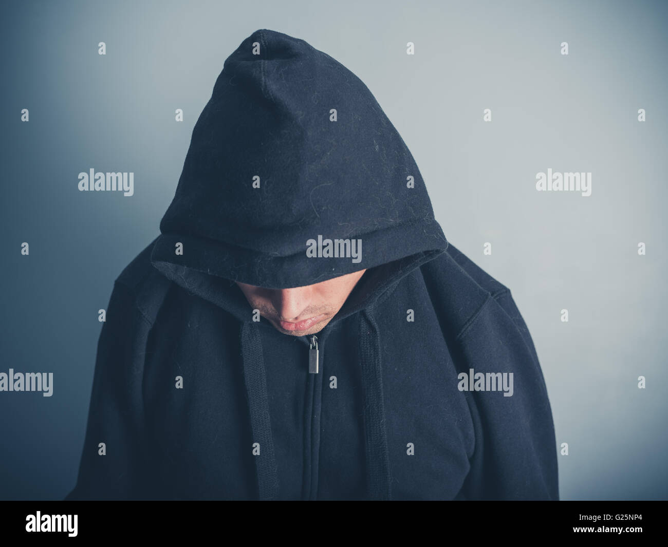 Un giovane uomo indossa un top con cappuccio e guardando verso il basso Foto Stock