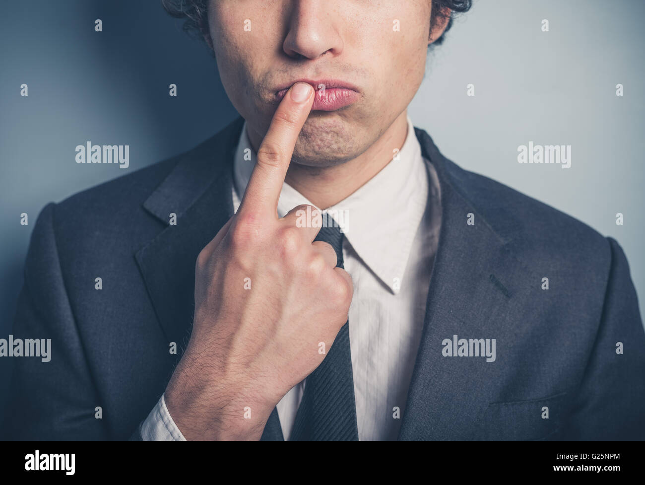 Un oculato imprenditore giovane con il suo dito sulle sue labbra Foto Stock