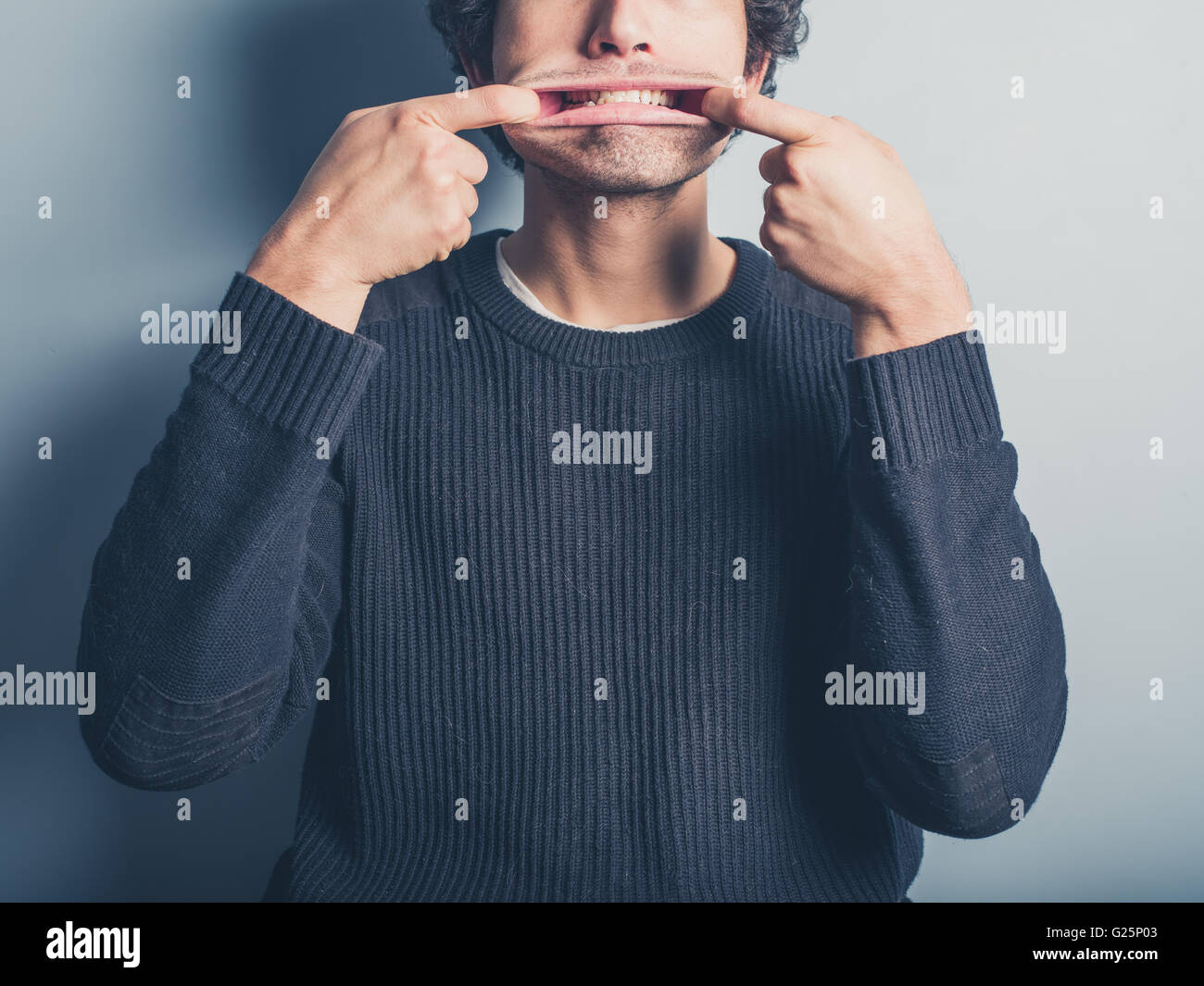 Un giovane uomo che indossa un maglione nero è tirando silly volti Foto Stock