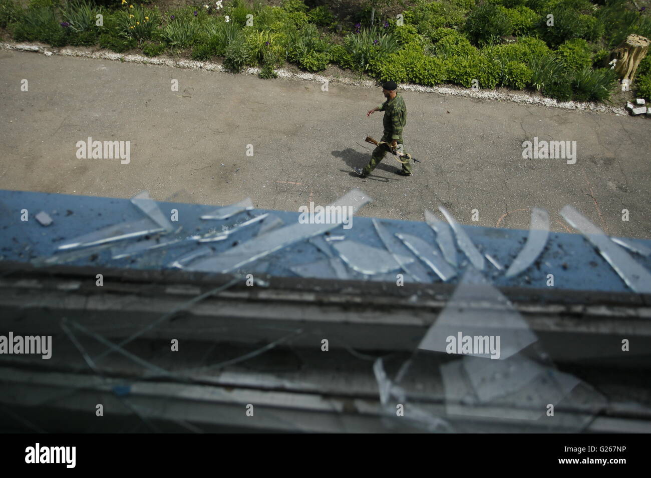 Donetsk, Ucraina. Xxiv Maggio, 2016. Un uomo armato passeggiate passato una finestra danneggiata in ribelli controllavano Staromykhaylivka village vicino a Donetsk, Ucraina, 24 maggio 2016. Il portavoce del Cremlino Dmitry Peskov ha confermato che la speciale missione di monitoraggio in Ucraina nel quadro dell'Organizzazione per la sicurezza e la cooperazione in Europa è in corso di discussione. Credito: Alexander Ermochenko/Xinhua/Alamy Live News Foto Stock