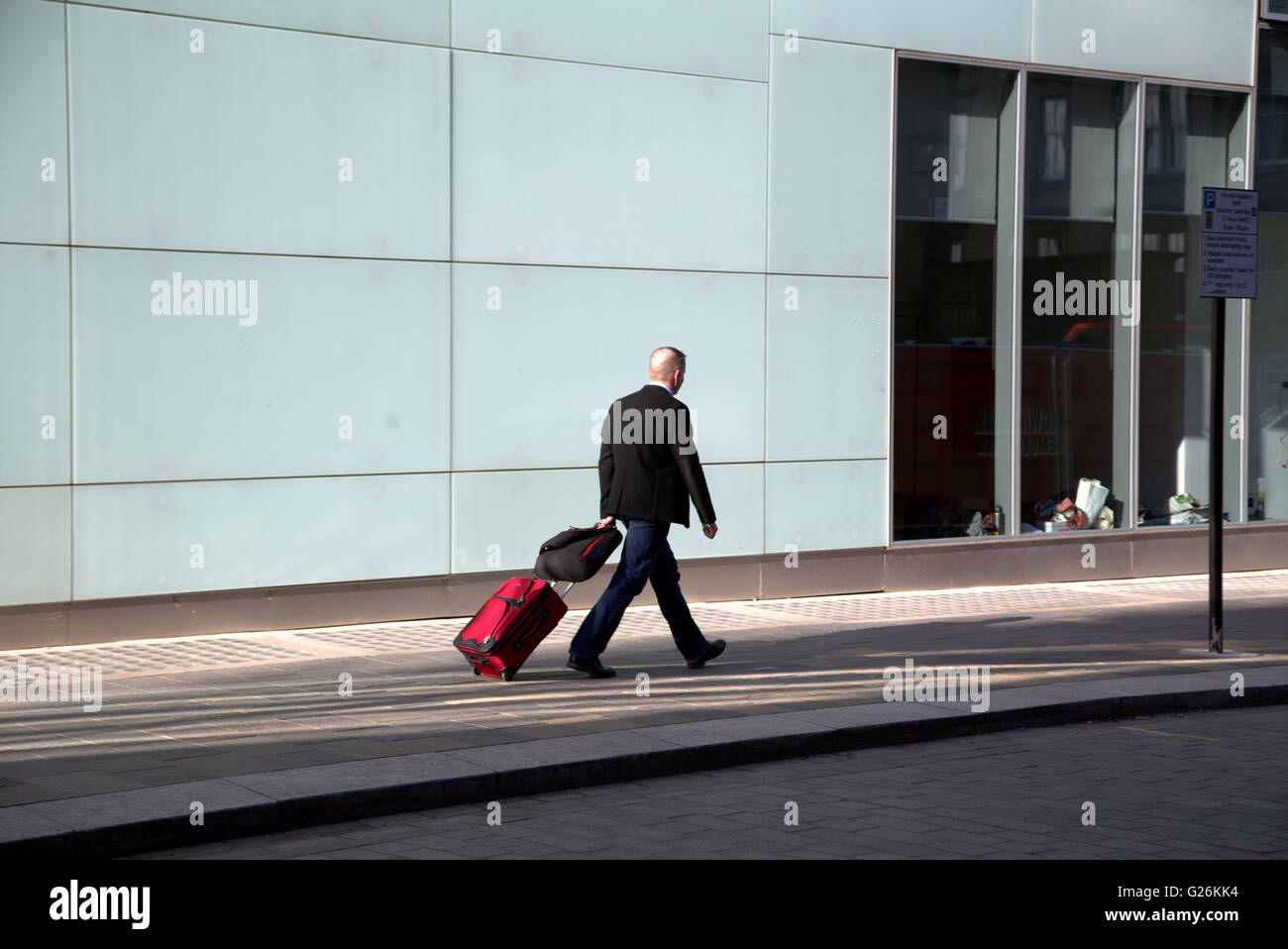 Giovane uomo a camminare con il caso contro sfondo modernista Glasgow, Scotland, Regno Unito.Glasgow Foto Stock