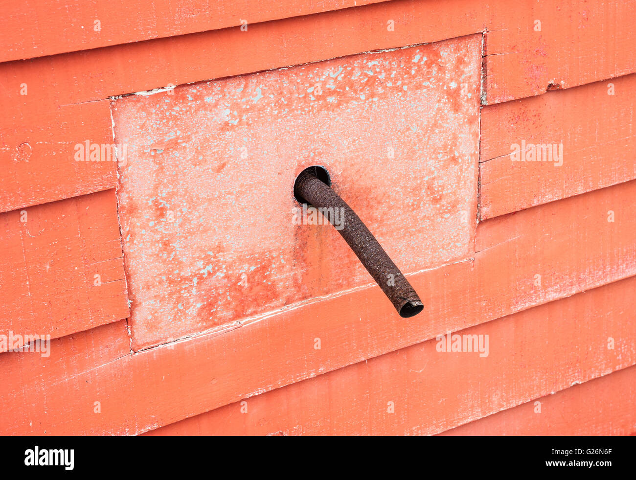 Vecchio arrugginito curva tubo metallico sporgente dal pannello quadrato nel muro rosso. Foto Stock