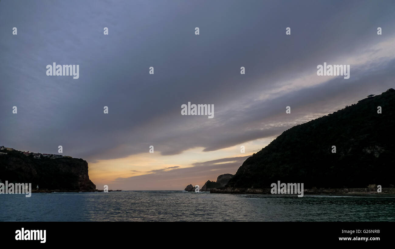 Cielo di tramonto knysna bay sud africa montagne ogni lato e il passaggio tra con cielo nuvoloso sfondo Foto Stock