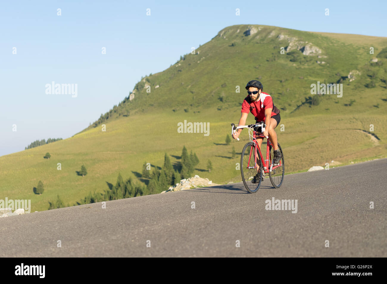 Ciclista sulla bici su strada salendo la collina in una giornata di sole Foto Stock