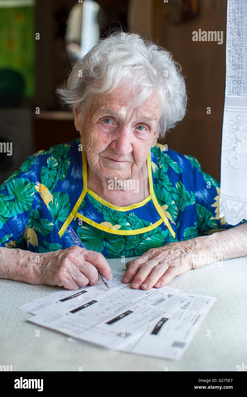Una donna anziana compila i moduli per il pagamento di servizi di pubblica utilità. Foto Stock