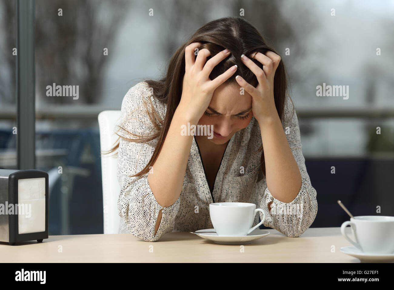 Triste e depresso donna da sola in un solitario bar dopo una pausa con una piovosa giornata invernale all'aperto in background Foto Stock