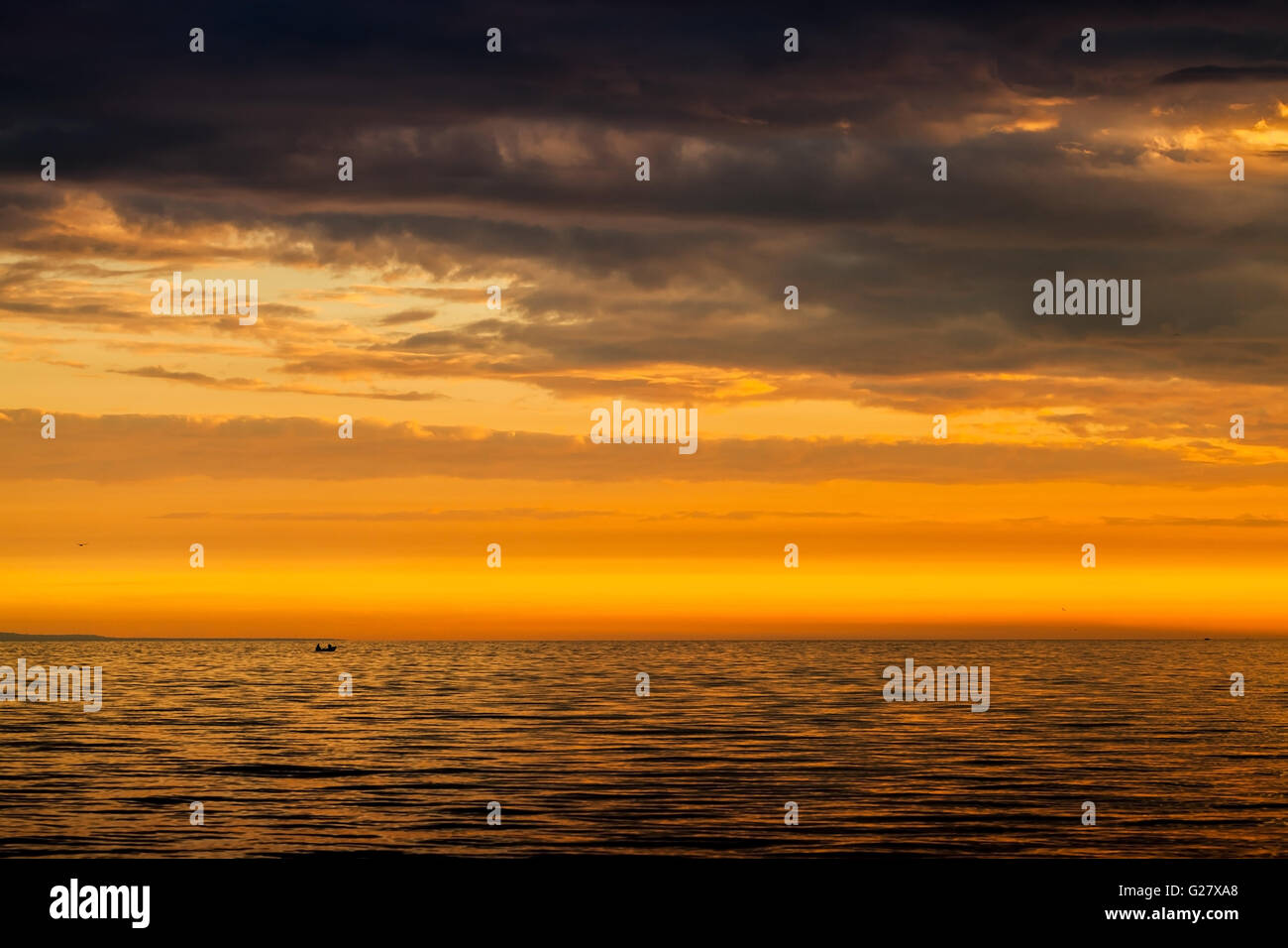 Drammatica cloudscape, luminoso tramonto sul Mar Baltico. Cielo nuvoloso, ancora acqua e pescatori su una piccola barca a distanza Foto Stock