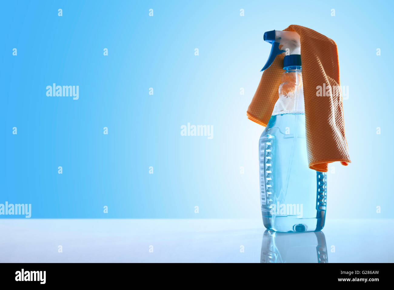 Bottiglia con un detergente per vetri e uno straccio giallo su un tavolo bianco vetro con sfondo blu panoramica. Vista frontale. Posizione orizzontale Foto Stock