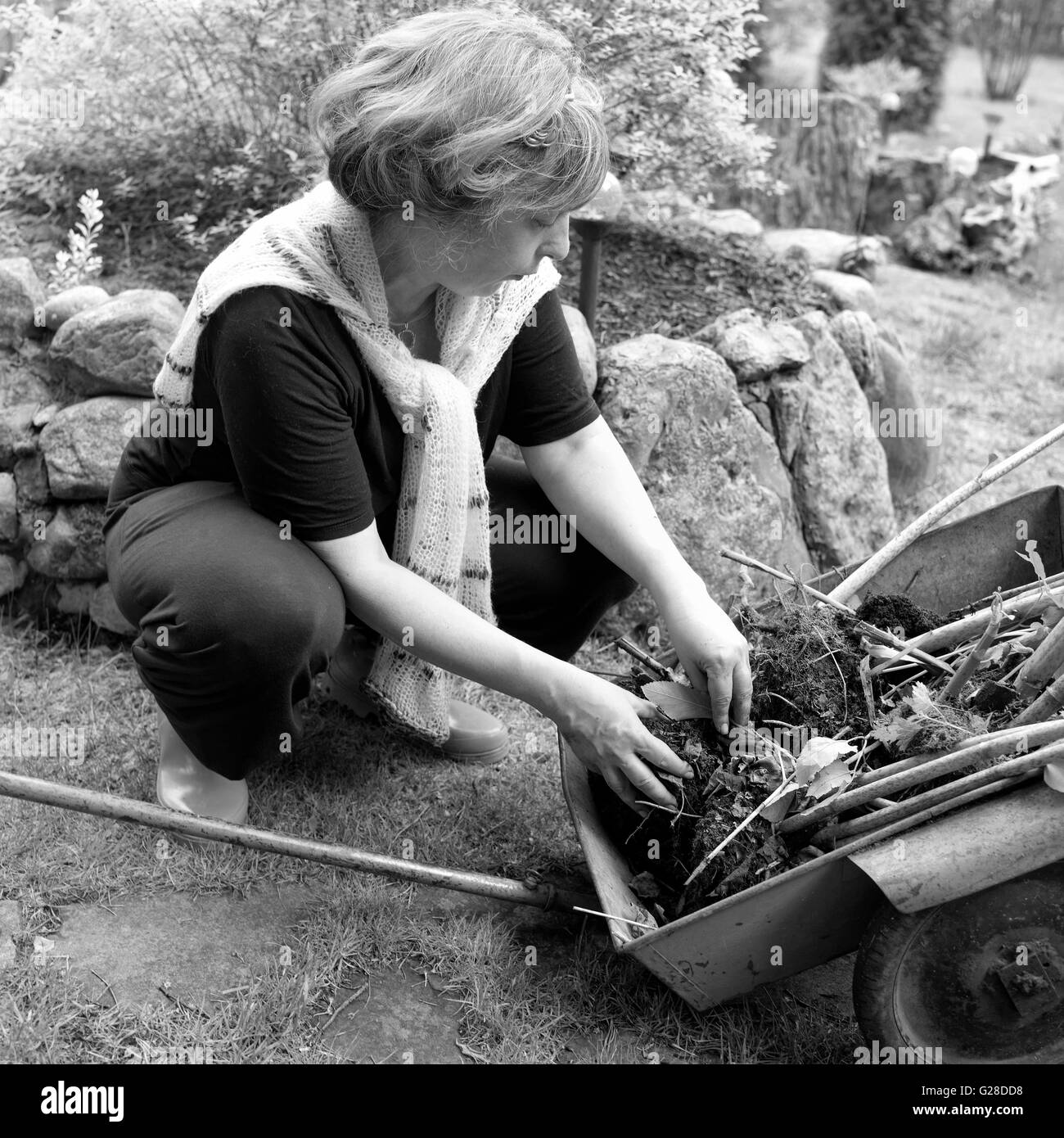 Carrello con piante in primo piano e la donna che lavorano nel suo giardino, piazza all'aperto girato in bianco e nero Foto Stock