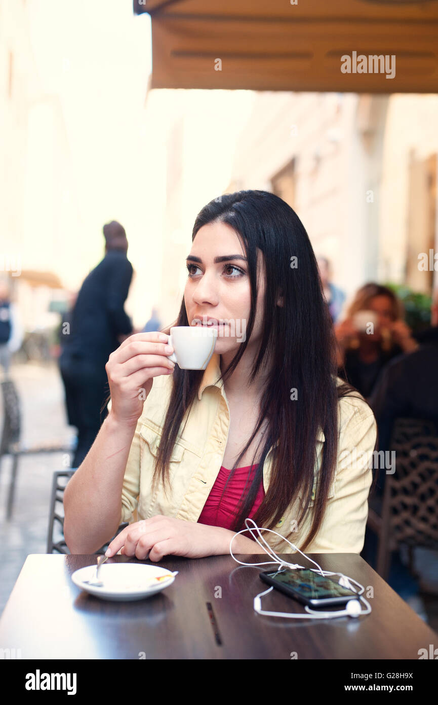 Giovane donna di bere il caffè in bar all'aperto in una strada di città seduta a tavola il tempo primaverile Foto Stock