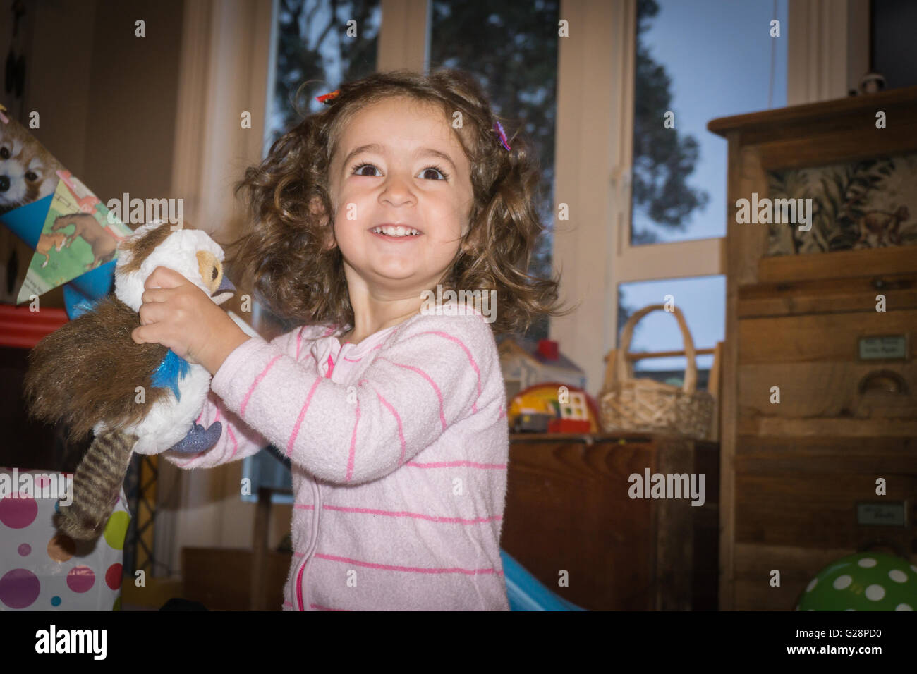 Compleanno mattina due anno vecchio ragazza ancora in pigiama nella lounge frizioni felicemente un giocattolo morbido bird presente che ha appena ricevuto. Foto Stock