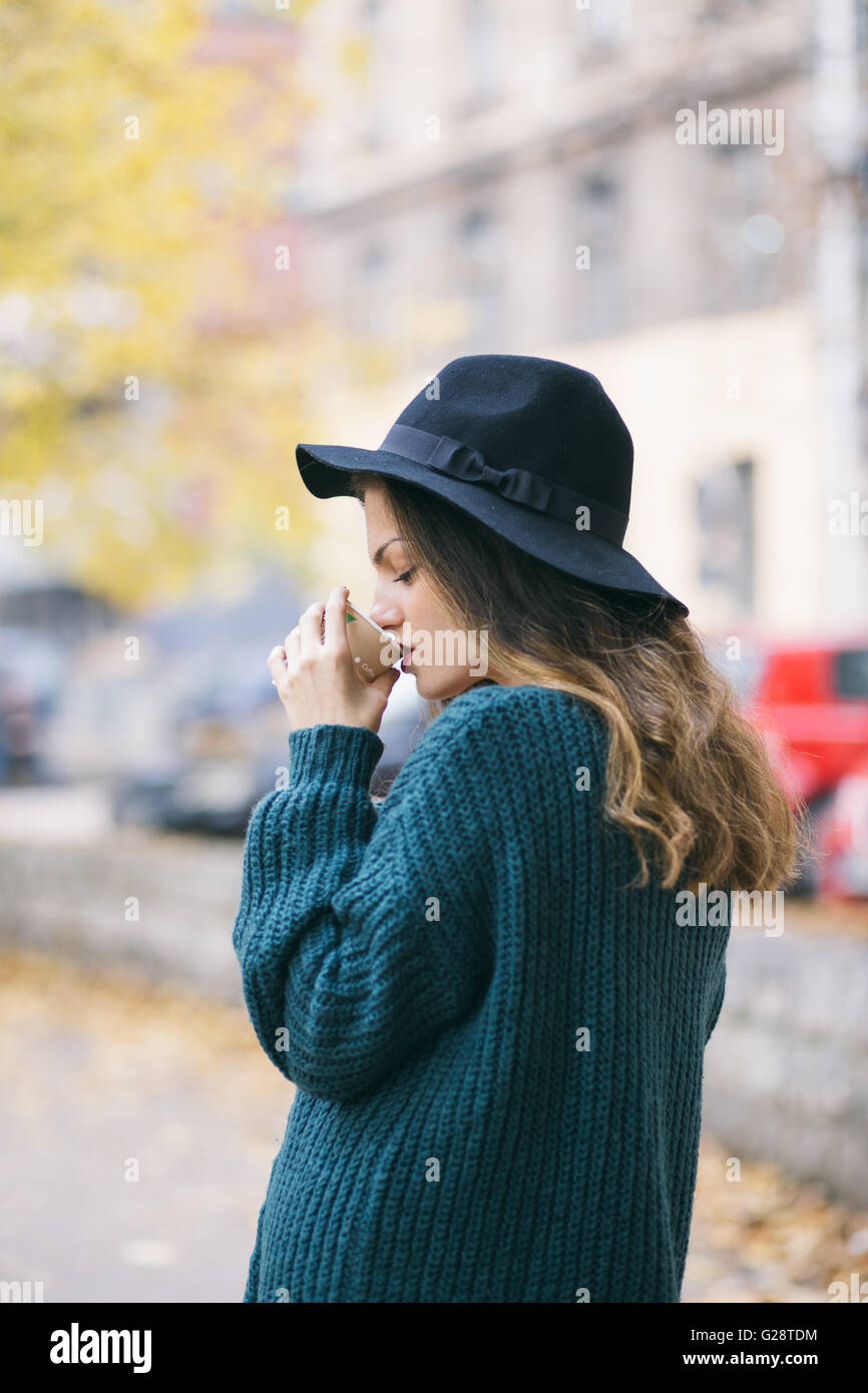 Giovane donna sulla strada con black hat di bere il caffè Foto Stock