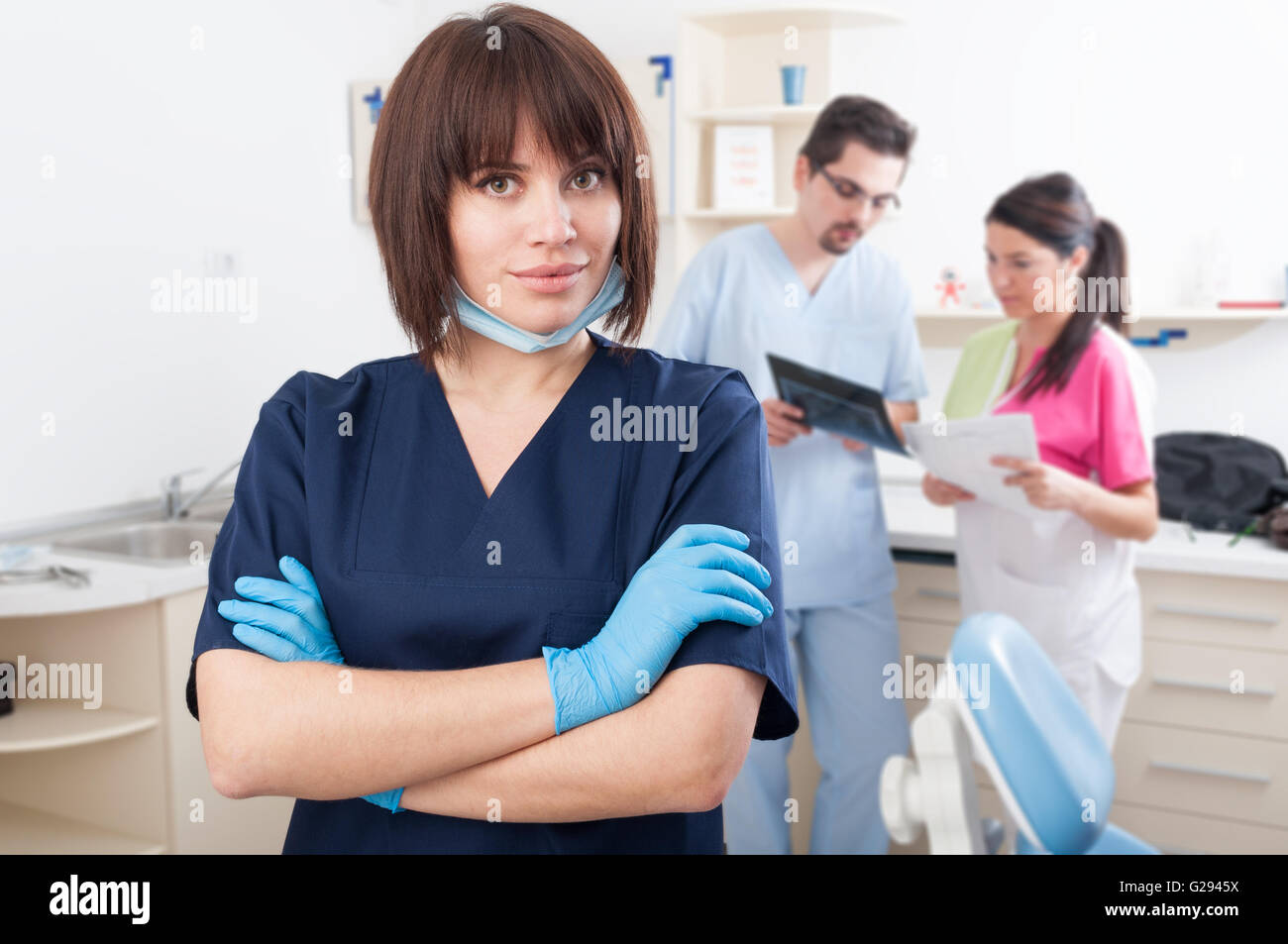 Fiducioso dentista donna sorridente nel fuoco in studio dentistico con assistenti dietro Foto Stock