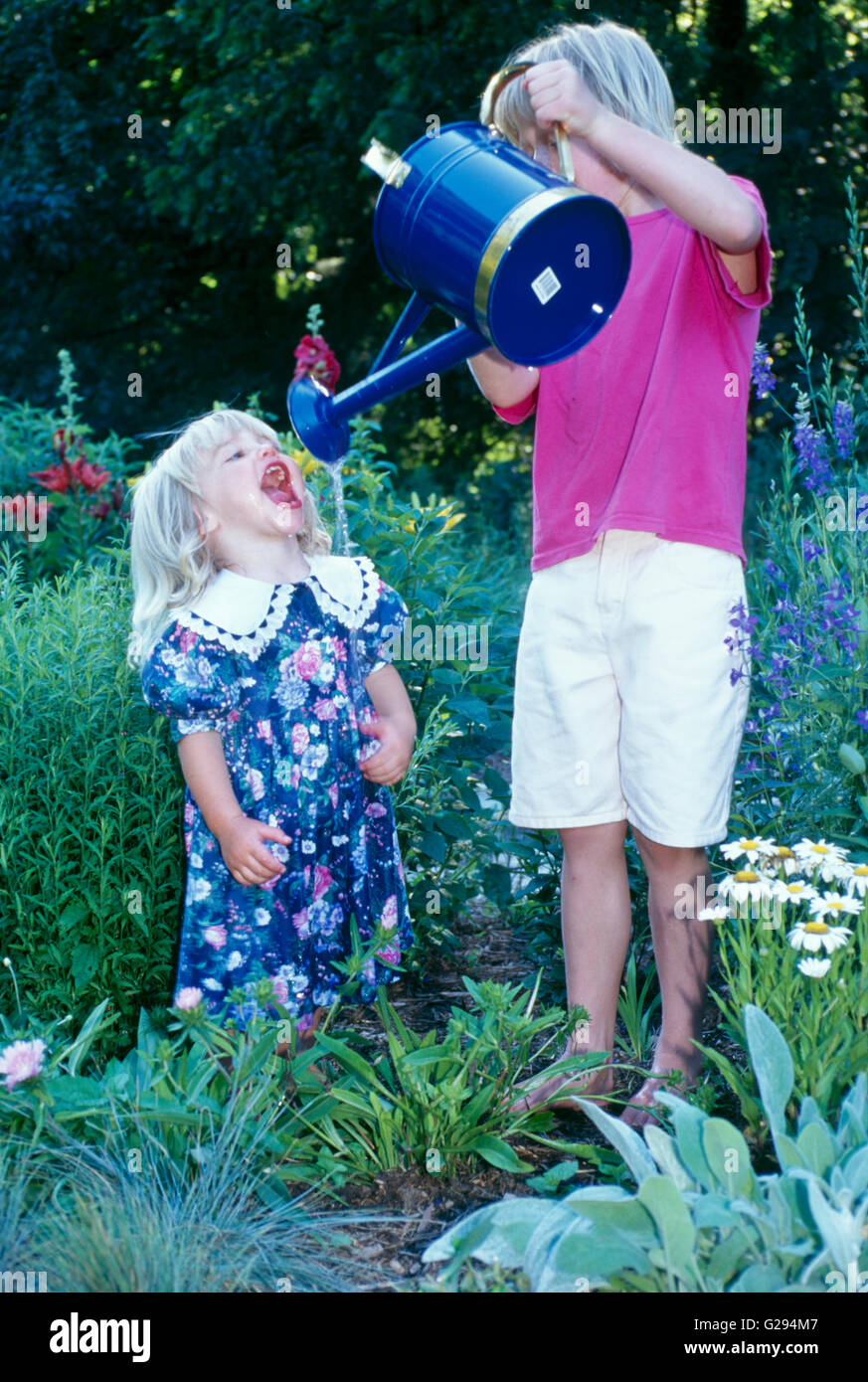 Due sorelle bionda giocando con annaffiatoio in estate giardino fiorito, Missouri, Stati Uniti d'America Foto Stock