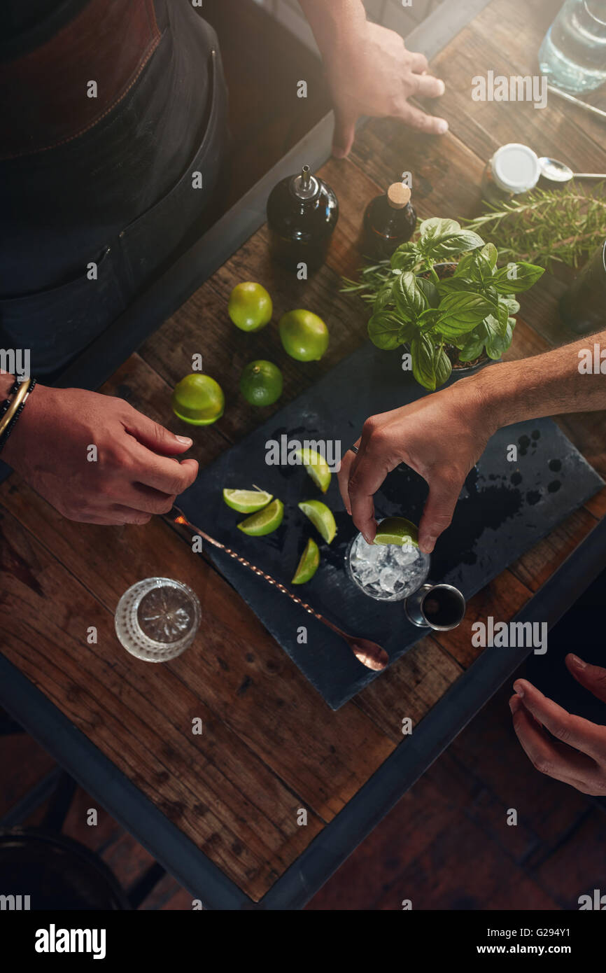 Primo piano delle mani di barman spremendo il limone in vetro. Due baristi preparano nuovi rinfrescanti cocktail presso il contatore. Foto Stock