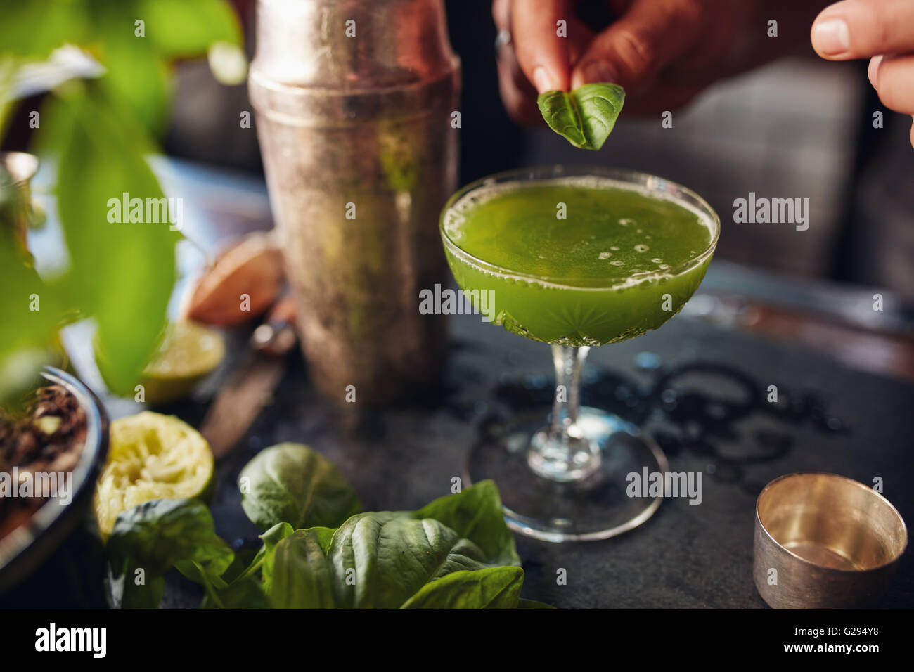 Immagine ravvicinata di barman farcitura verde fresco cocktail con una foglia di basilico. Il barman prepara il basilico smash cocktail. Foto Stock