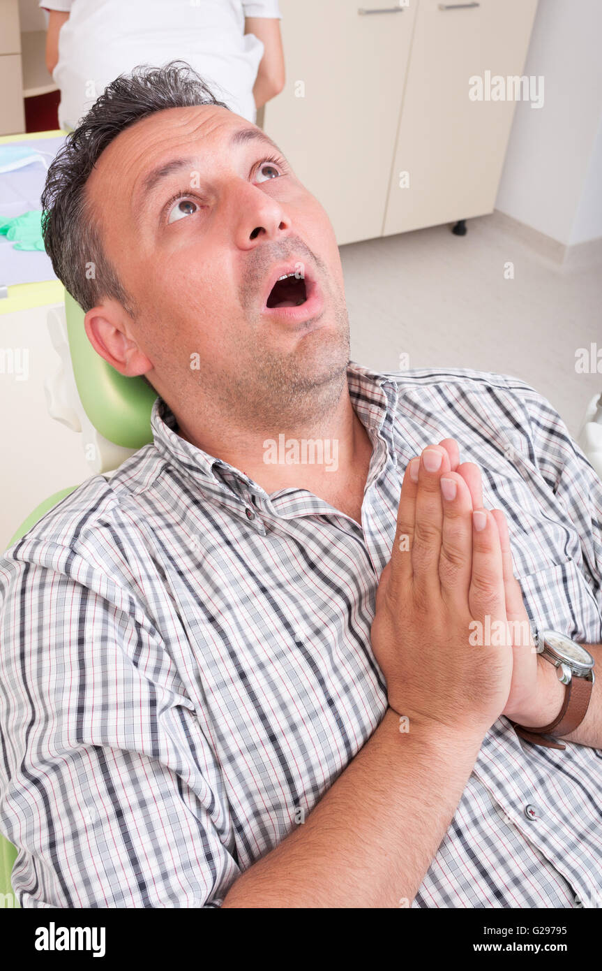 La paura del dentista concetto con un paziente uomo che prega sulla poltrona del dentista. Foto Stock