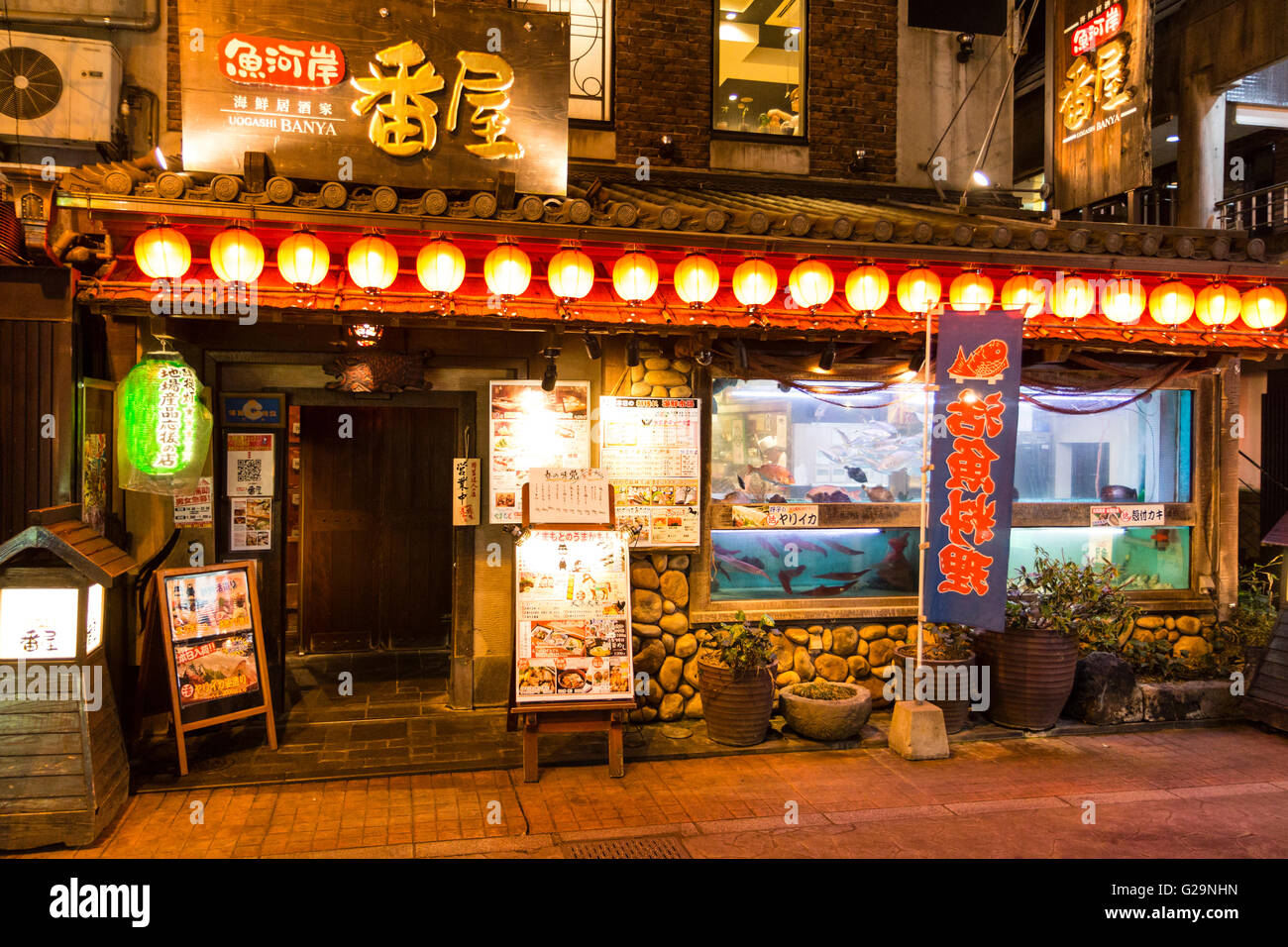 Giappone Kumamoto, Centro citta'. Di sera. Parte anteriore di uno stile tradizionale giapponese ristorante di frutti di mare, Uogashi Banya, con pesci che nuotano in serbatoi in finestra.. Foto Stock