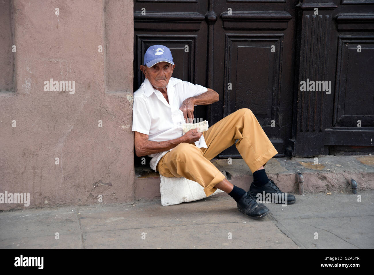 Ritratto di un cubano uomo seduto alla porta della sua casa a Cienfuegos Cuba contando il suo denaro Foto Stock