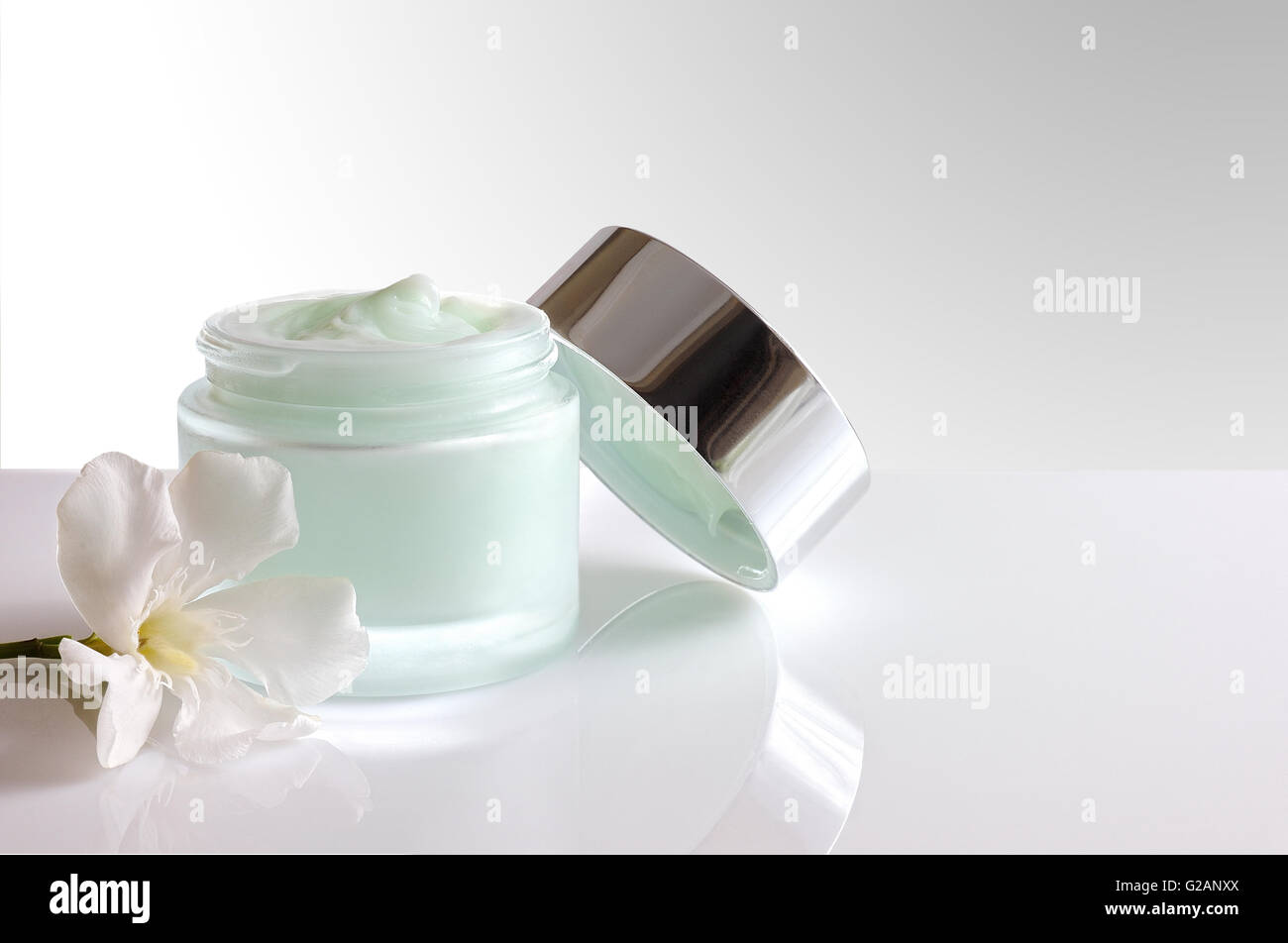 Vetro vaso aperto con trattamento viso o crema per il corpo sul tavolo bianco con coperchio e fiore. Bianco sfondo isolata . Vista frontale. Foto Stock