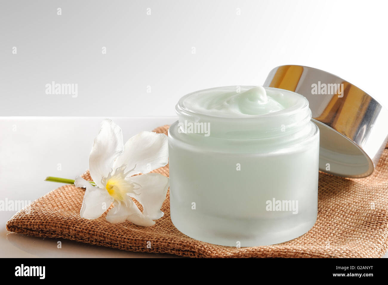 Vetro vaso aperto con viso o corpo crema sulla tela. Con coperchio e fiore.sfondo isolato. Vista frontale. Foto Stock