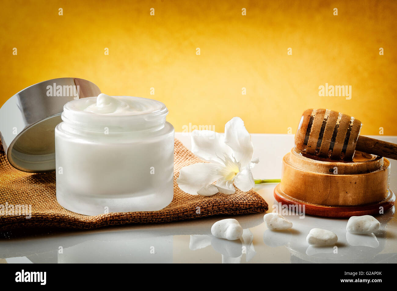 Aprire il vaso di vetro con miele idratante isolato su bianco tavolo in vetro. Fiore, tela e la canna da zucchero con miele contenitore decorazione. Foto Stock