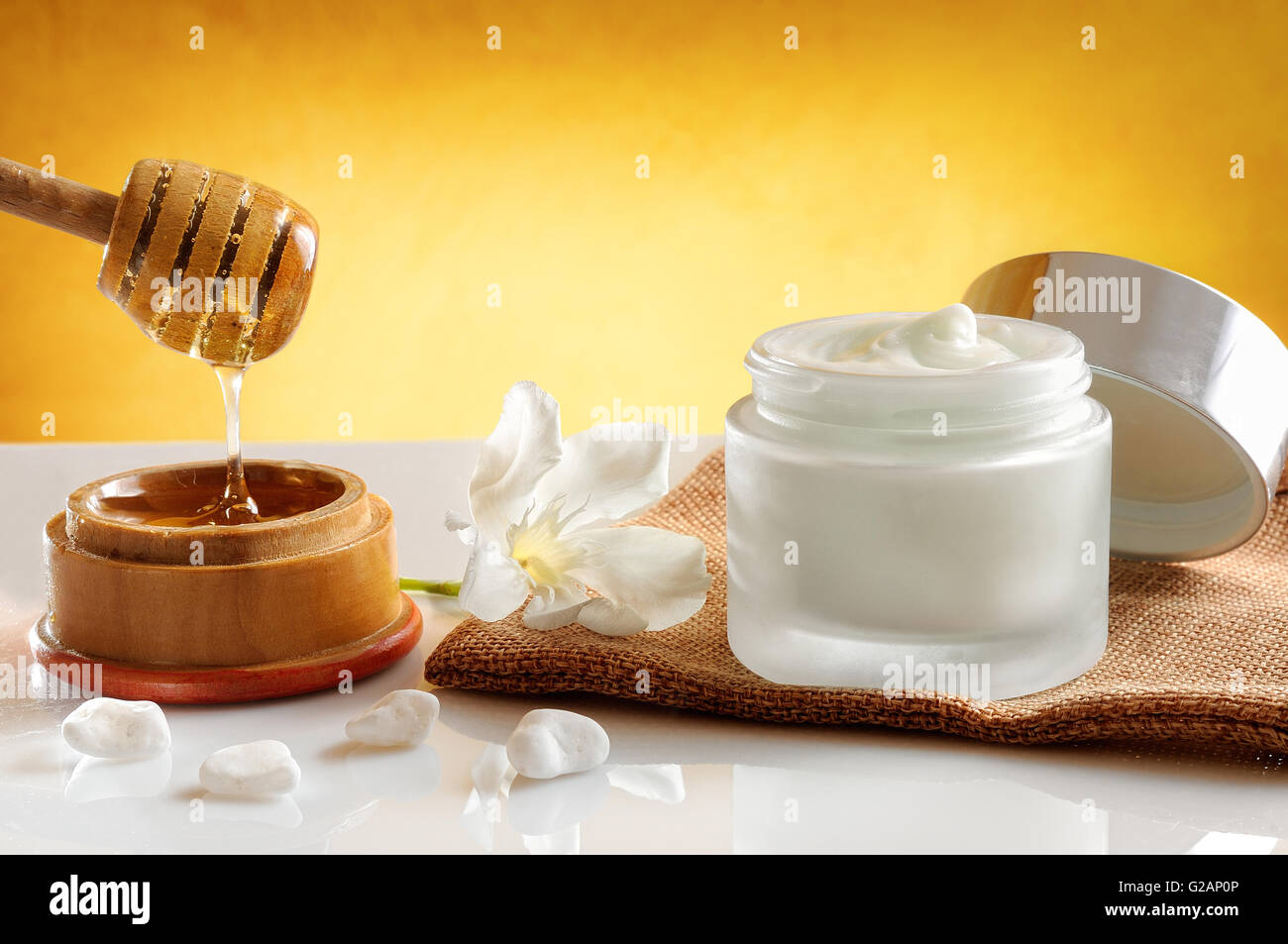 Aprire il vaso di vetro con miele idratante isolato su bianco tavolo in vetro. Fiore, tela e la canna da zucchero con miele contenitore decorazione. Foto Stock