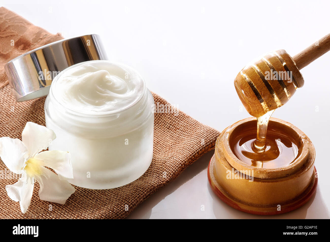 Aprire il vaso di vetro con miele idratante isolato su bianco tavolo in vetro. Fiore, tela e la canna da zucchero con miele contenitore decorazione. Foto Stock