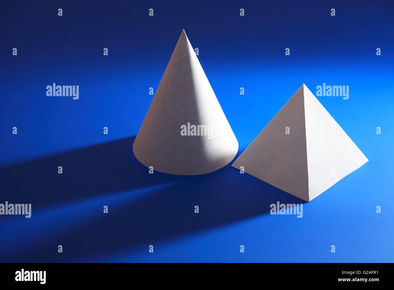 Concetto di geometria. Libro bianco cono vicino a piramide su sfondo blu Foto Stock