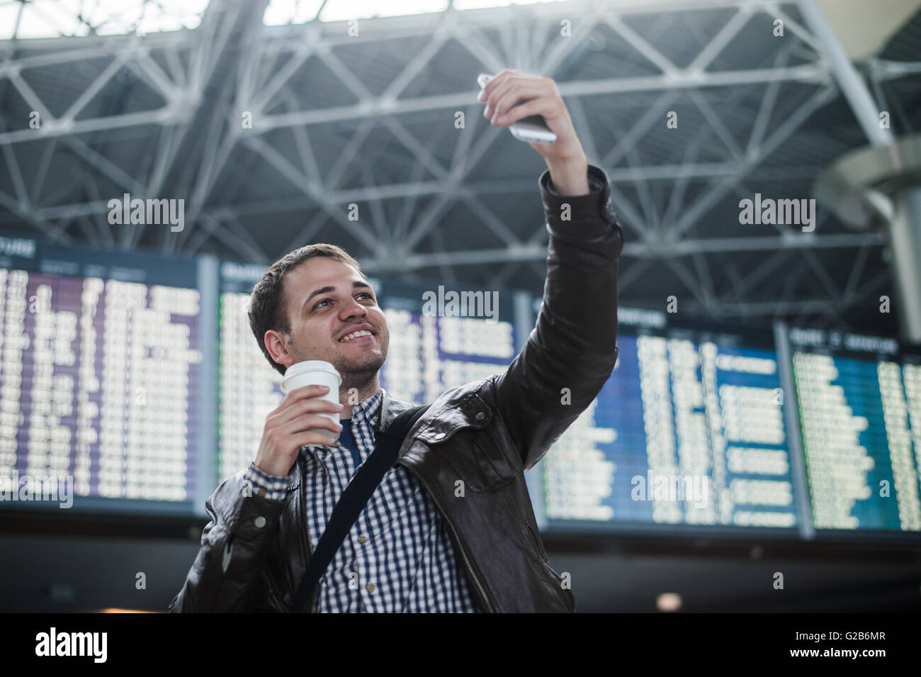 Sorridente giovane viaggiatore uomo con un caffè presso l'aeroporto rende selfie nella parte anteriore della scheda calendario Foto Stock