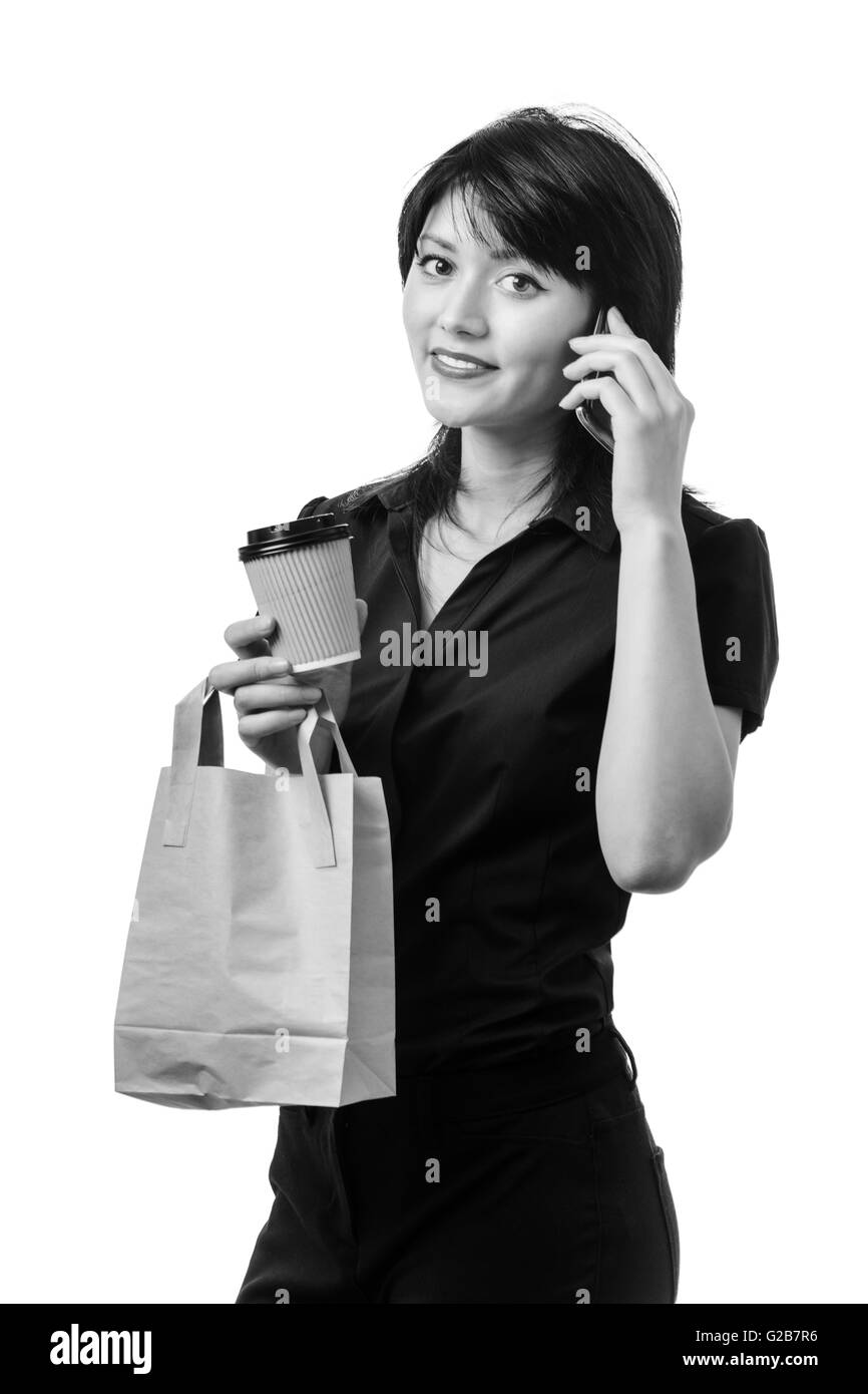 Studio shot di una giovane donna di affari tenendo un sacchetto di carta per un pranzo e monouso per bevande da asporto cup e parlando sul suo mo Foto Stock