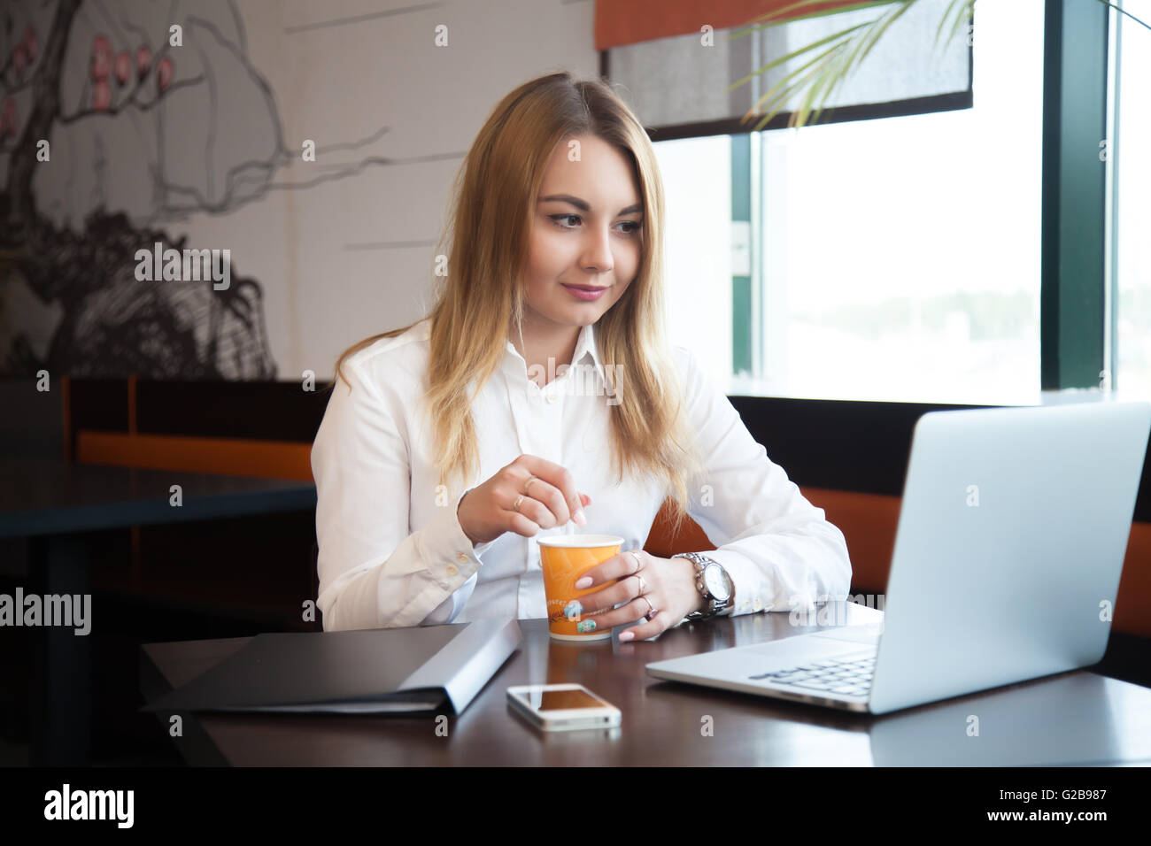 Giovani belle ufficio caucasica donna formale di usura alla moda in seduta urbana moderna cafe agitando la sua bevanda Foto Stock