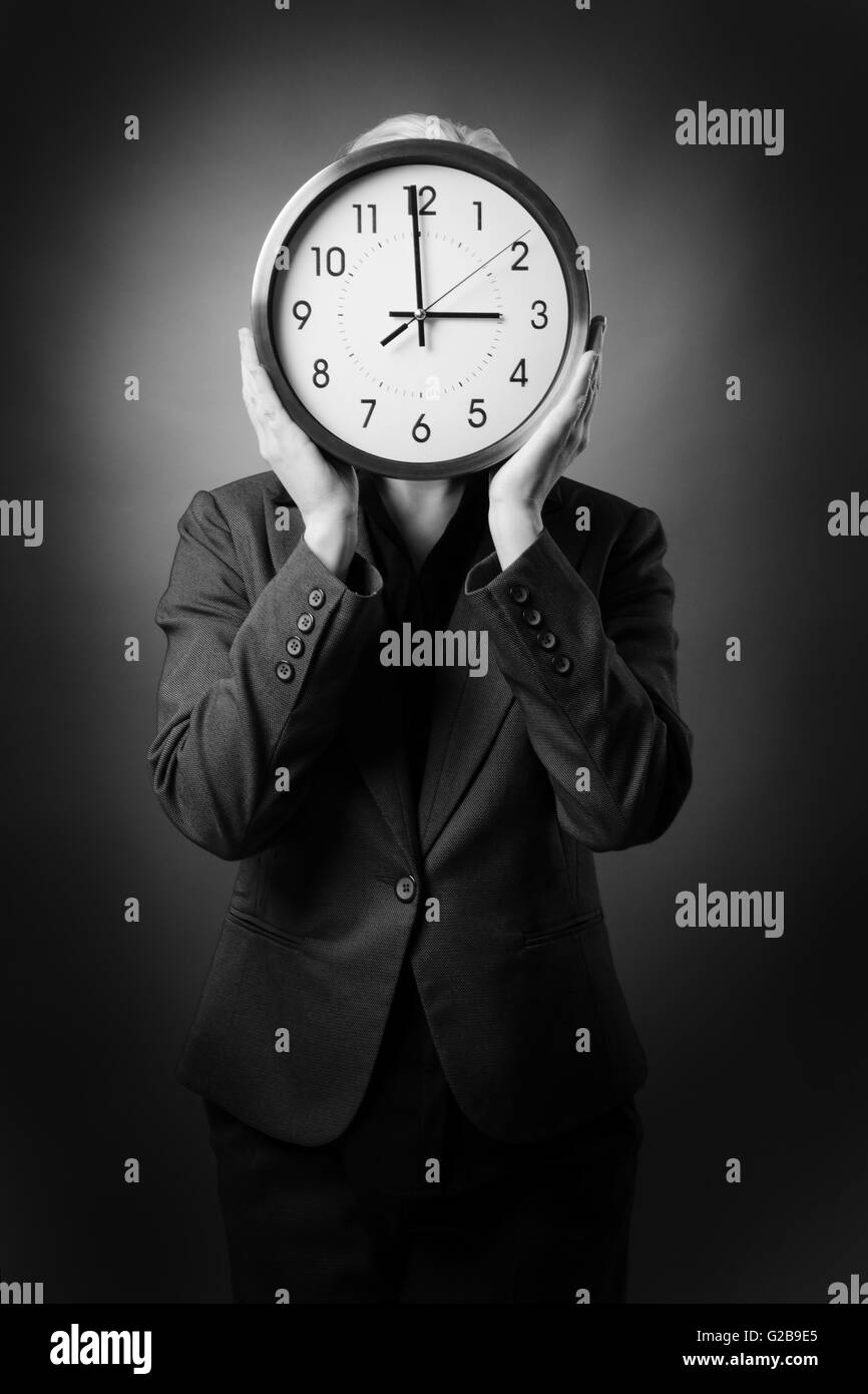 Business donna in un vestito tenendo un rotondo grande orologio numerico davanti al suo volto, shot su sfondo bianco Foto Stock