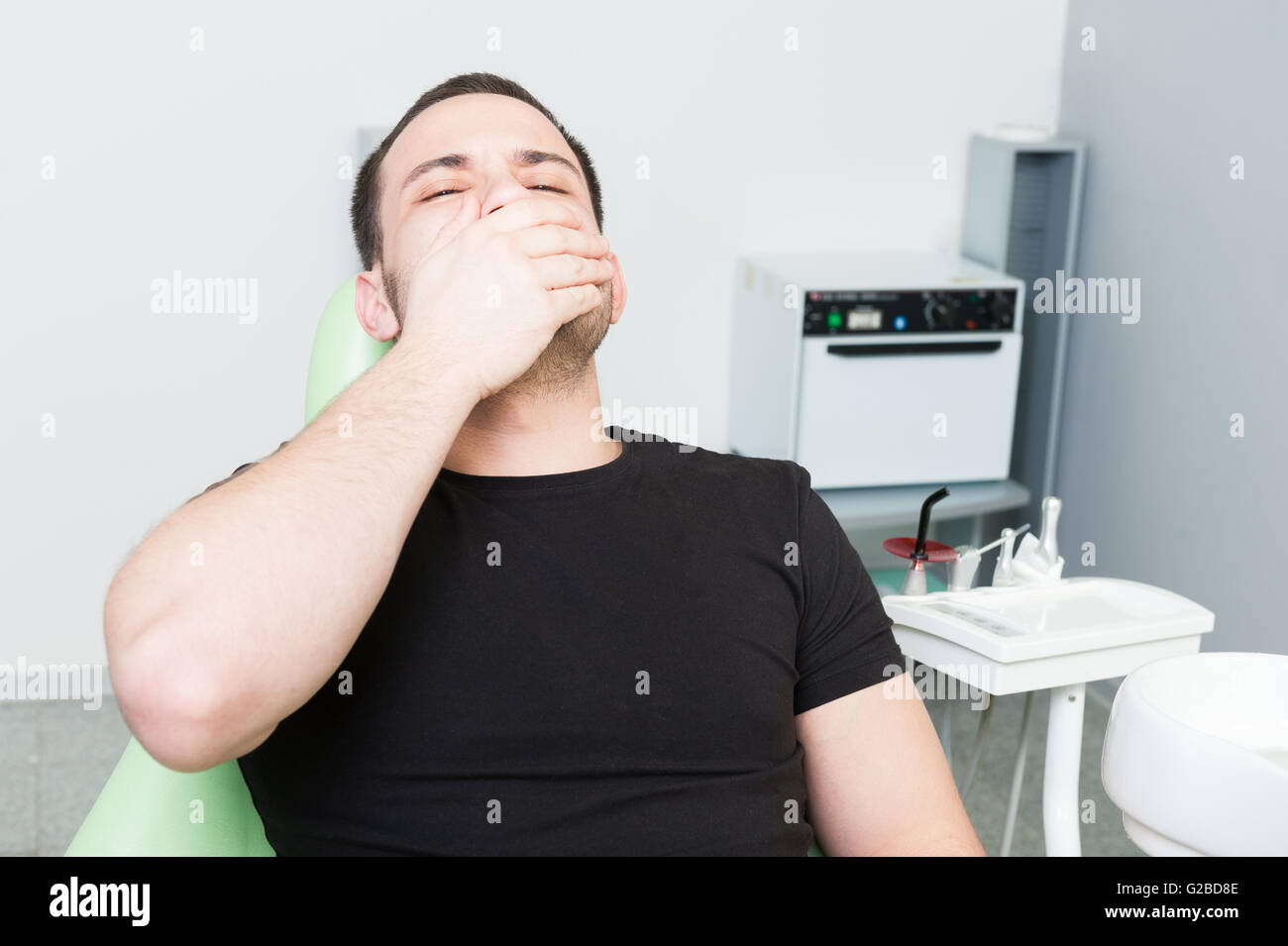 Spaventata paziente di sesso maschile al dentista che copre la sua bocca e la sensazione di dolore di denti Foto Stock