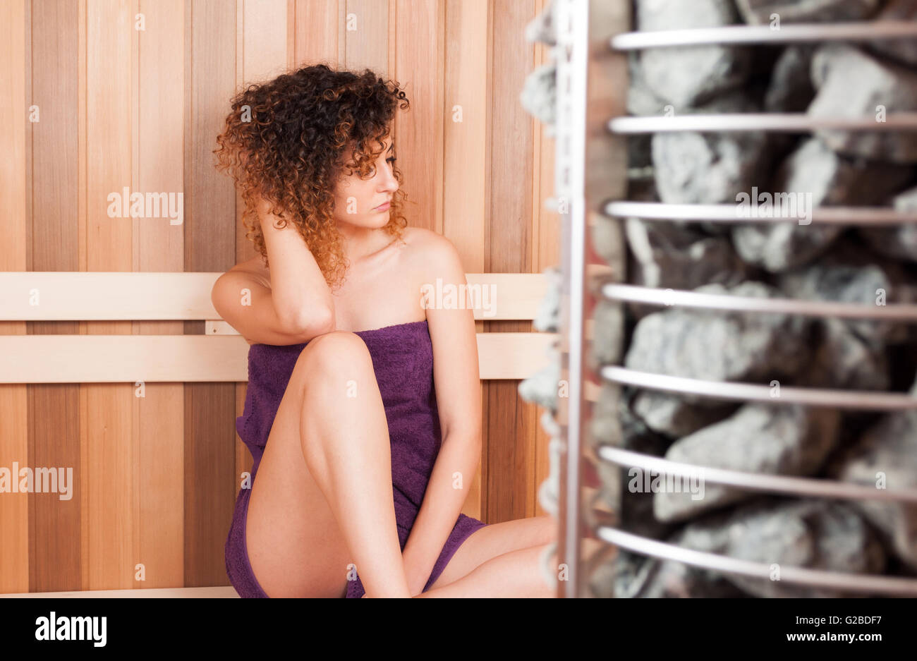 Bella donna seduta su un banco di lavoro accanto al forno sauna rilassante e appoggiata Foto Stock
