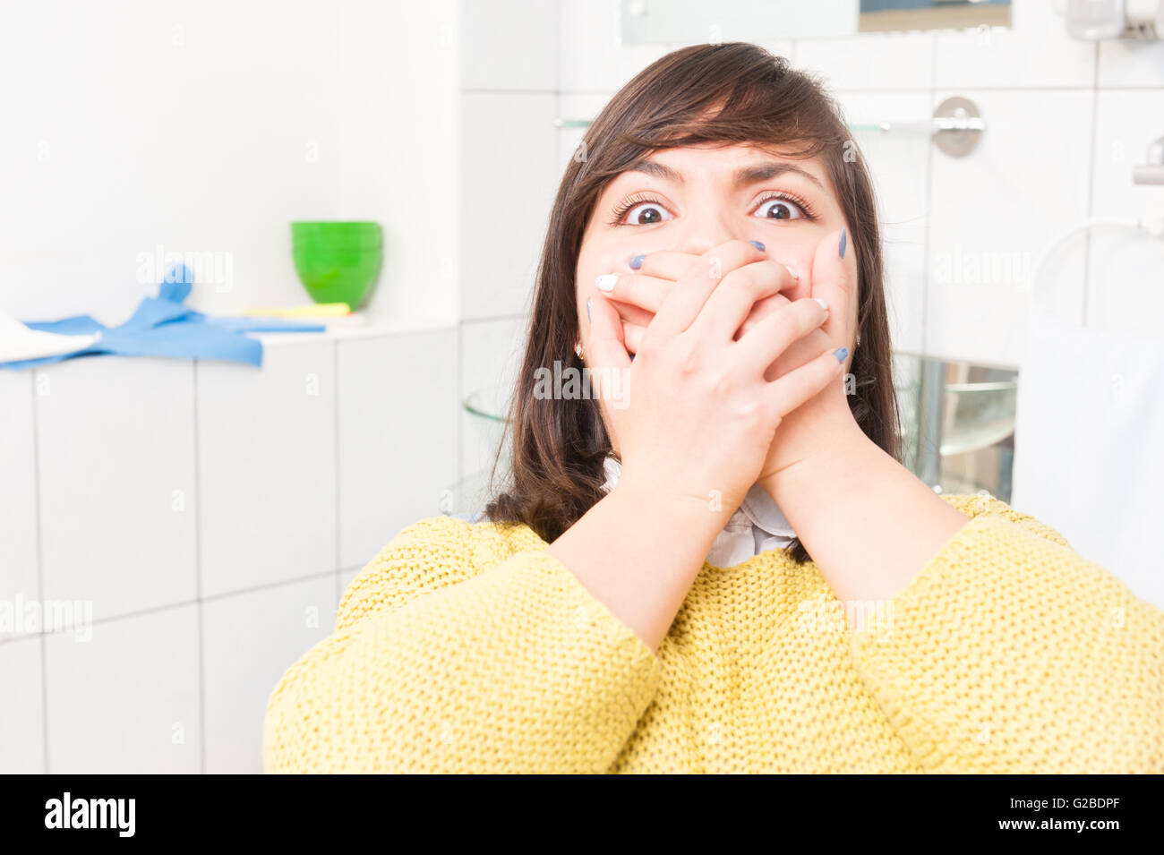 Close-up ritratto di donna terrorizzata spaventata al dentista visita seduti in poltrona e che copre la bocca Foto Stock