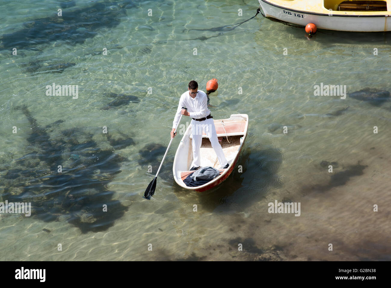 DUBROVNIK Croazia un uomo vestito di bianco pantaloni e camicia usando una racchetta per spostare il suo dinghy in tutta la Città Vecchia porto Foto Stock