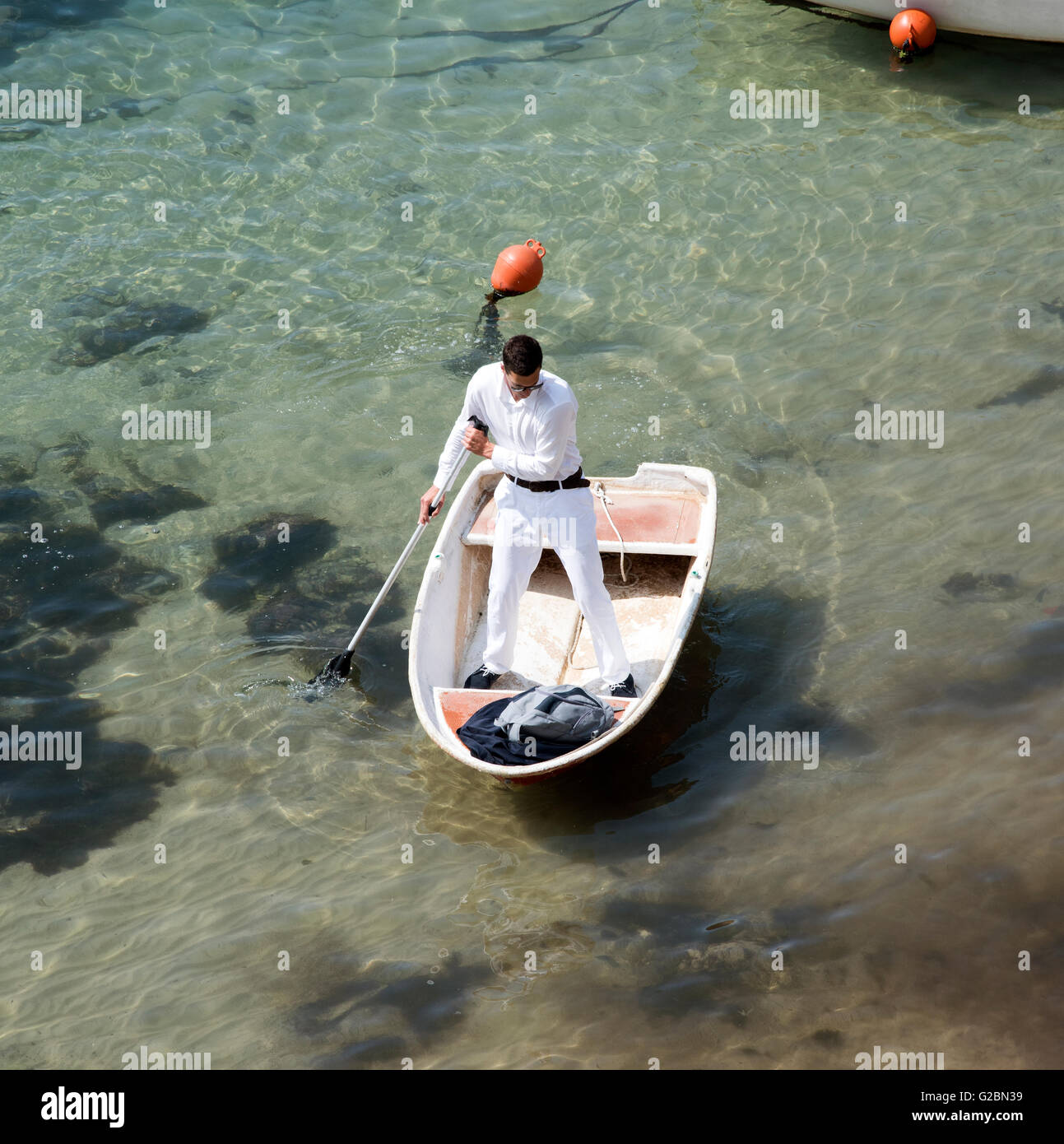 DUBROVNIK Croazia un uomo vestito di bianco pantaloni e camicia usando una racchetta per spostare il suo dinghy in tutta la Città Vecchia porto Foto Stock