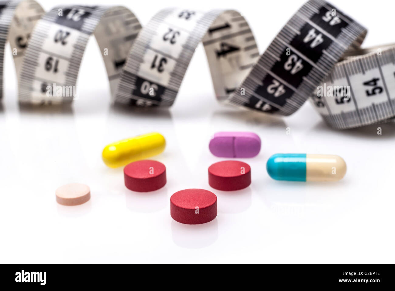 Colore pillole per la dieta con nastro di misurazione su sfondo bianco Foto Stock