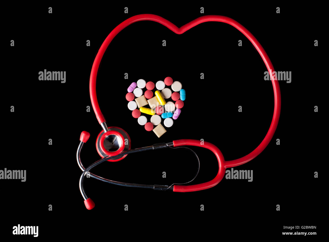 Forma di cuore Coloerd pillole medicina su sfondo nero con rosso stehoscope Foto Stock