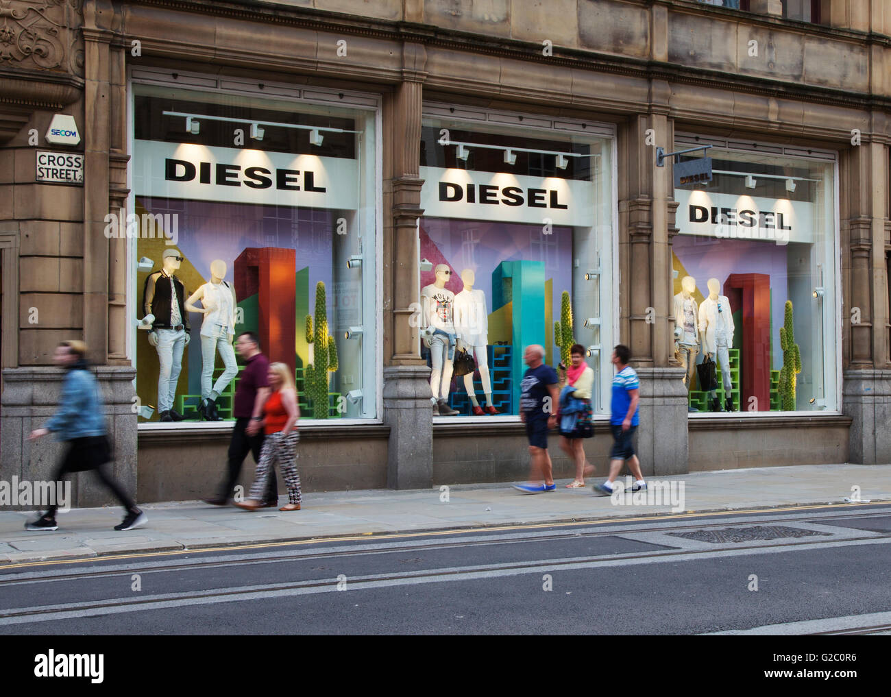 Persone che passano le vetrine del business retail negozi di moda nel centro della citta'. Negozio Diesel in Cross Street, Greater Manchester, Regno Unito Foto Stock