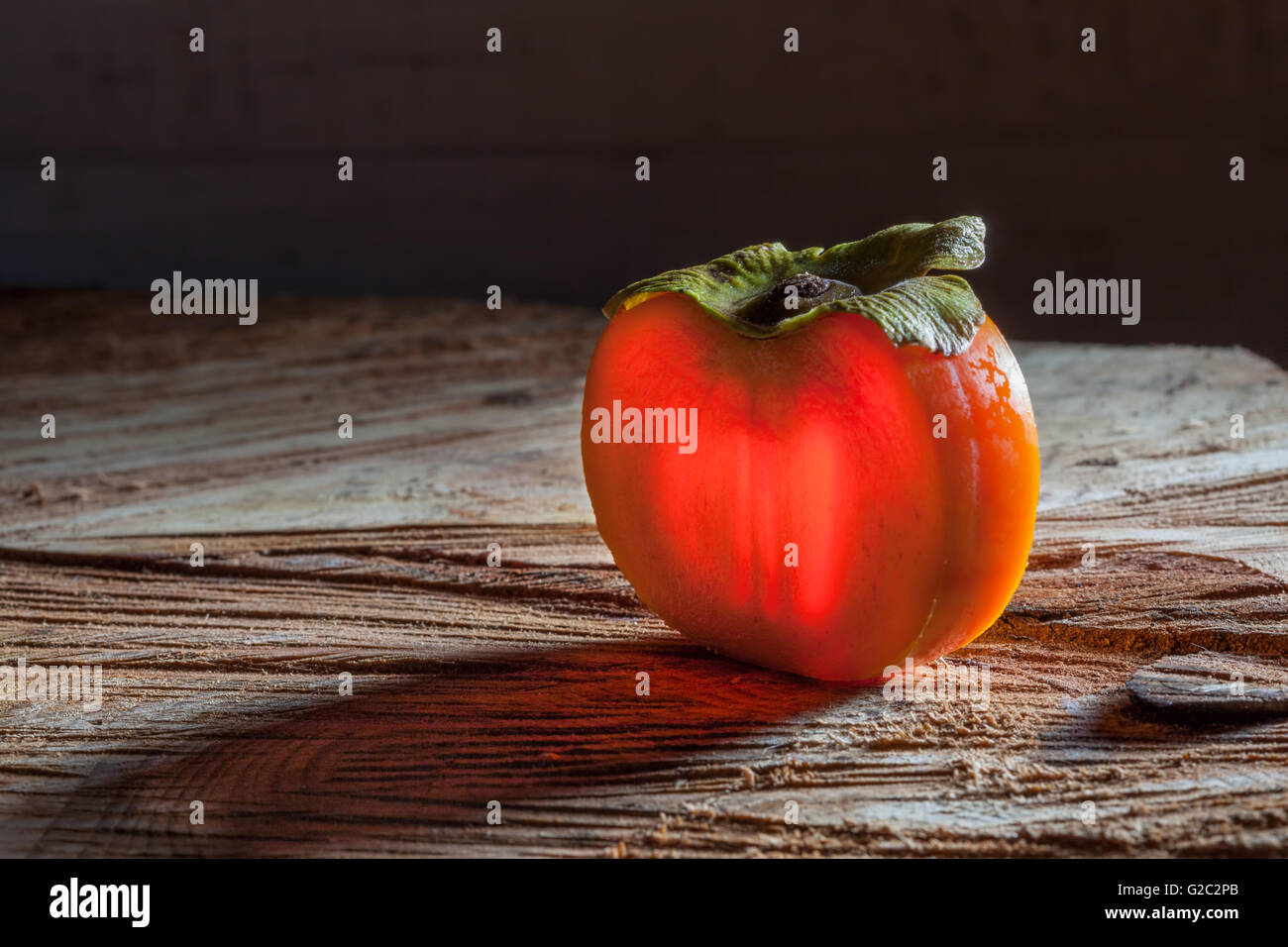 Fetta di persimmon incandescente nella luce arancione sulla ruvida la superficie di legno Foto Stock