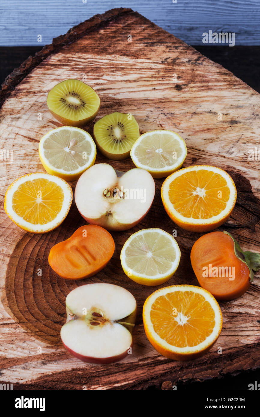 Fette di vari frutti sul taglio fresco di un moncone di legno. Kiwi, arancio, Apple, limone e persimmon Foto Stock