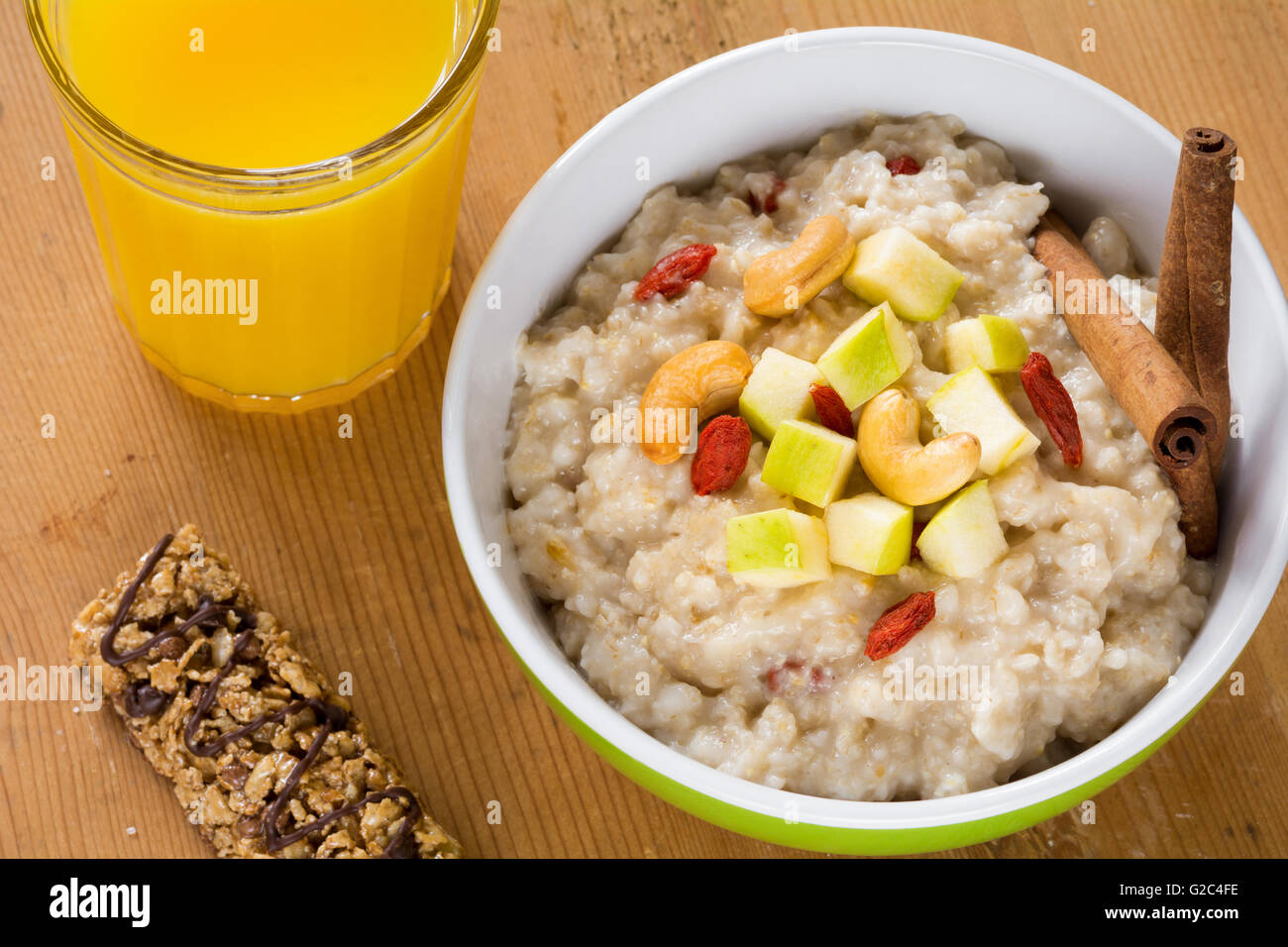 Porridge di fiocchi d'avena con mele, cannella, dadi e goji bacche. Barre di muesli, frutta fresca e succhi di arancia su sfondo di legno Foto Stock