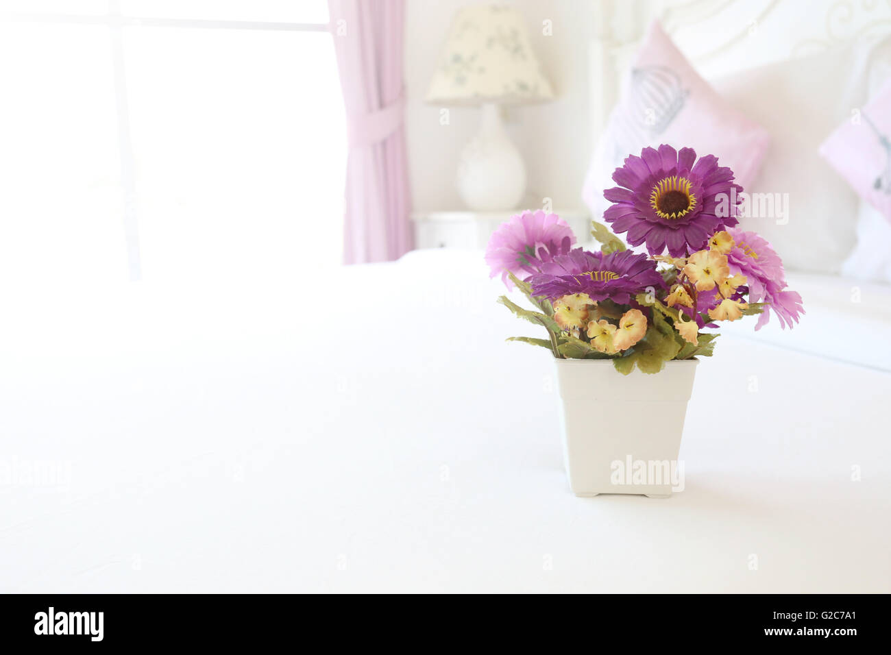 Vintage rosa fiori artificiali su un tavolo nella camera da letto bianco concetto interno per la progettazione dello sfondo. Foto Stock